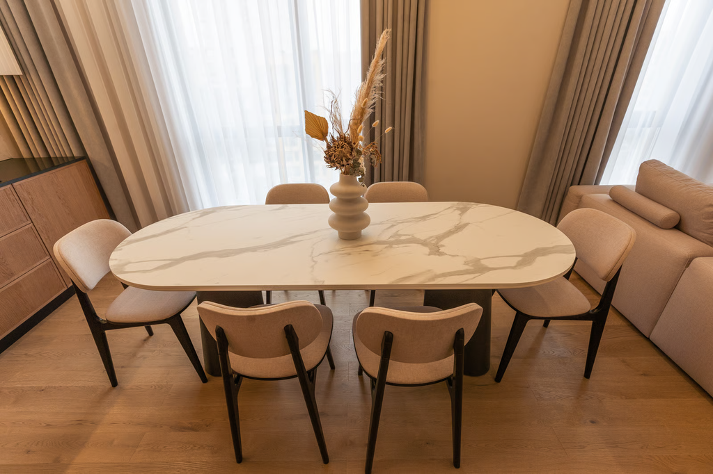 Meja makan minimalis dengan permukaan keramik motif batu alam berwarna krem pada ruang makan modern.