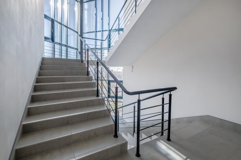 Tangga rumah dua lantai dengan bordes luas sebagai area transisi dan railing pengaman modern